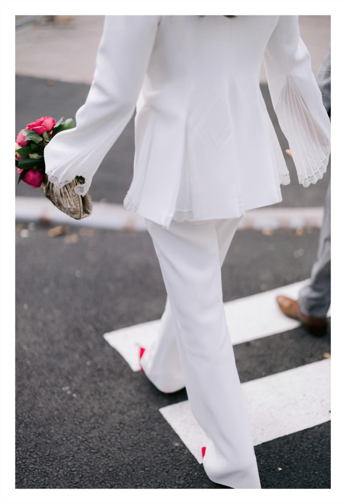 detail shot of a bride wearing a pantsuit and carrying a bright pink bouquet of flowers that match her bright pink heels