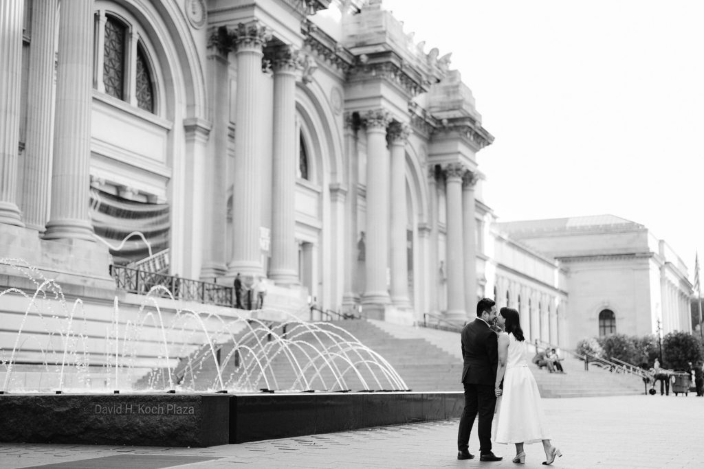 Engaged man and woman kiss in front of a fountain in New York City