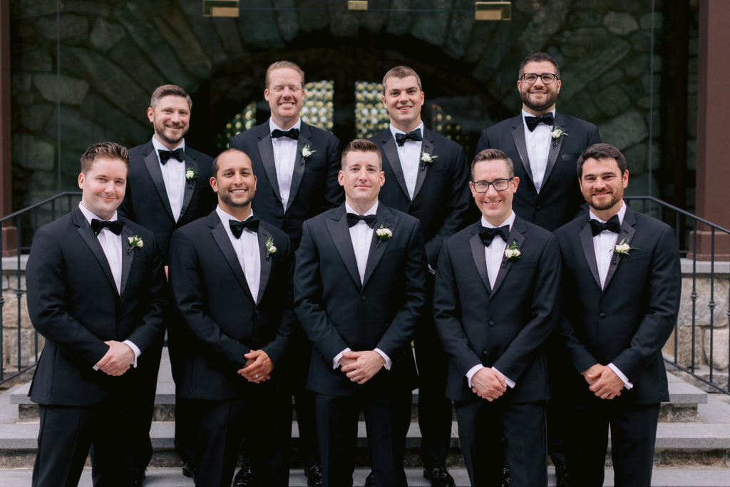 A groom and his groomsman pose in front of Le Chateau wedding venue in South Salem New York
