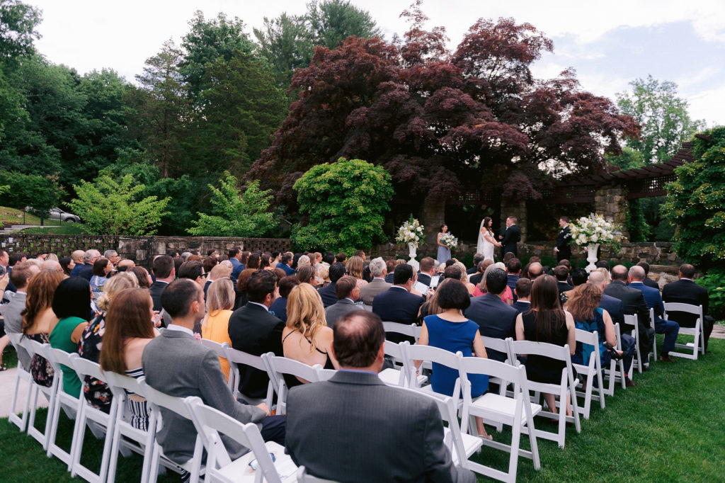 Guests look on as a bride and groom say their vows outside in the gardens at the popular Le Chateau wedding venue in South Salem, NY