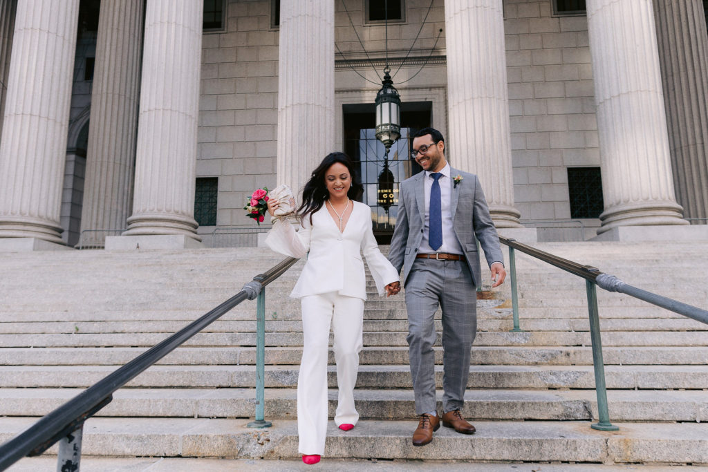 Newly married husband and wife come down the steps of city hall in New York City after their chic NYC elopement