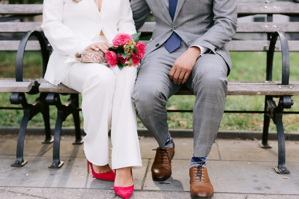 close up of a man and woman who are newlyweds sitting on a park bench with her bright pink bouquet matching her bright pink high heels