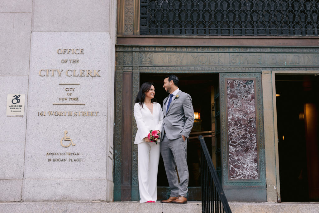 newlywed man and woman stand on the steps of New York City Hall after eloping