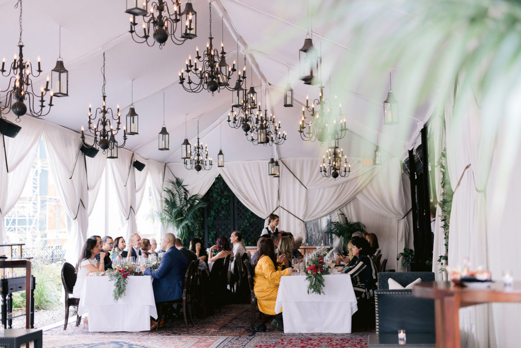 Wedding guests dine at the Nomad Hotel below ceiling draperies and chandeliers at this chic NYC elopement