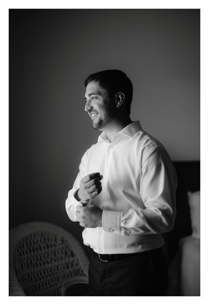 man smiles as he buttons his shirt preparing for his wedding. Jenny Fu Photography