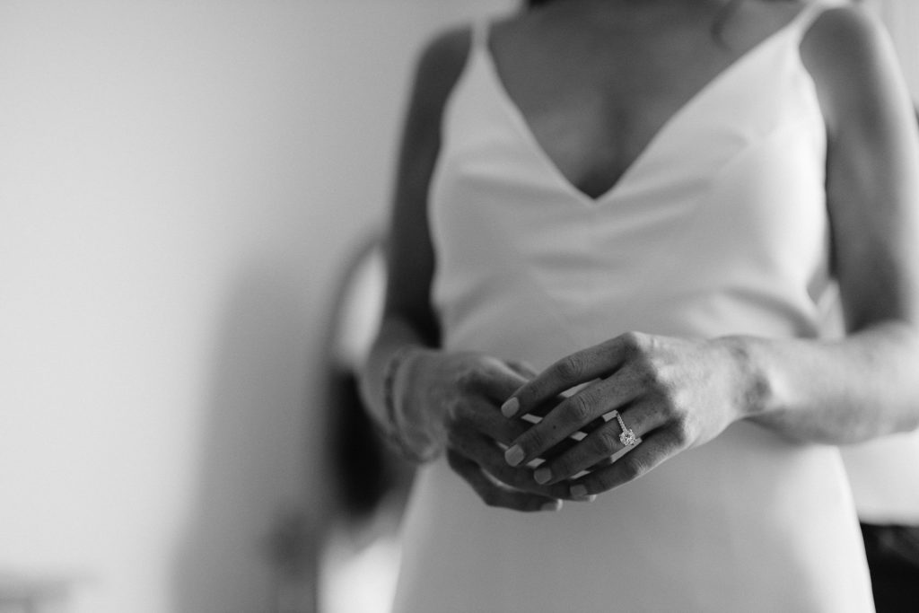 close up shot of the bride's hands and large engagement ring with ther simple, elegant strapped dress behind them