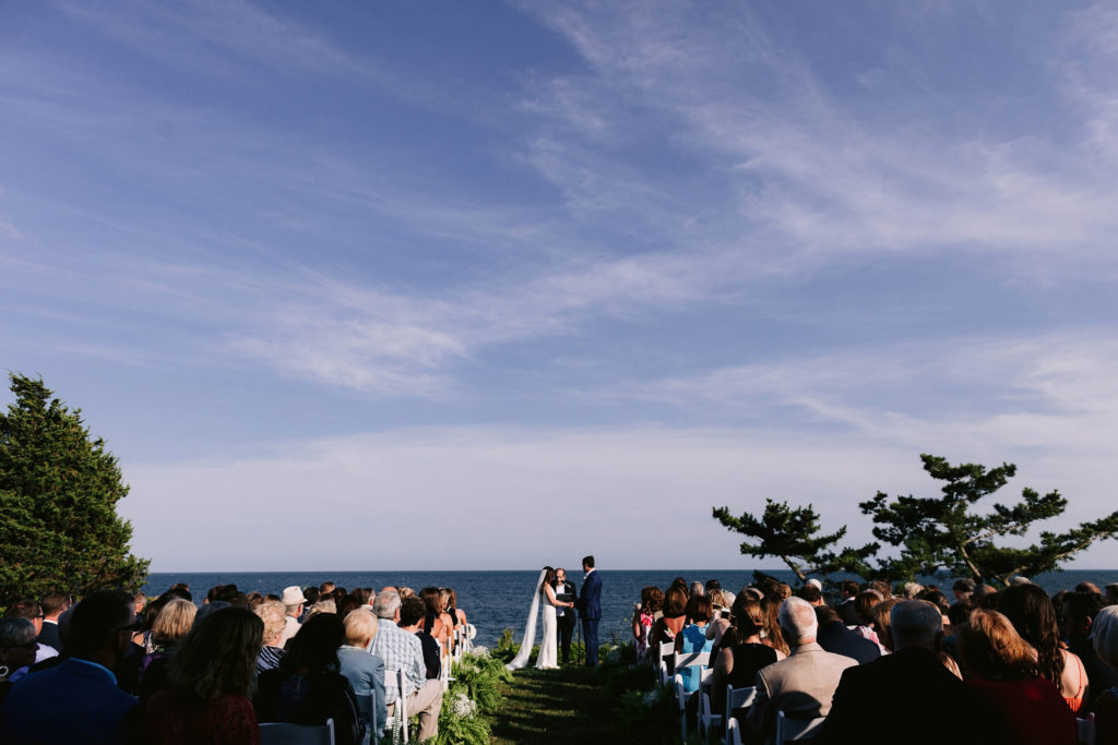 wide angle photo of wedding guests and bride and groom at this outdoor oceanside cape cod ceremony