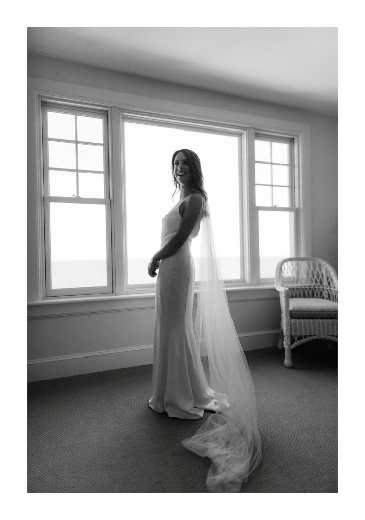 full length shot of a gorgeous brunette wearing a floor-length wedding dress and a cathedral veil standing in front of a large window