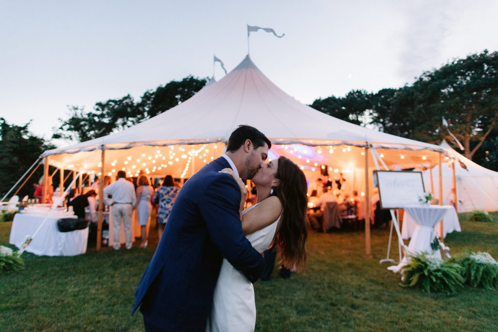 bride and groom make out happily in front of their reception tent during their festive, oceanside cape code wedding. PHoto by Jenny Fu photography