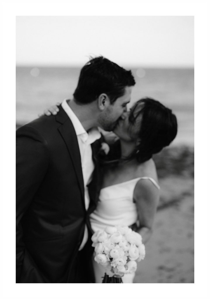 black and white of bride and groom kissing on the beach at cape cod after their wedding ceremony