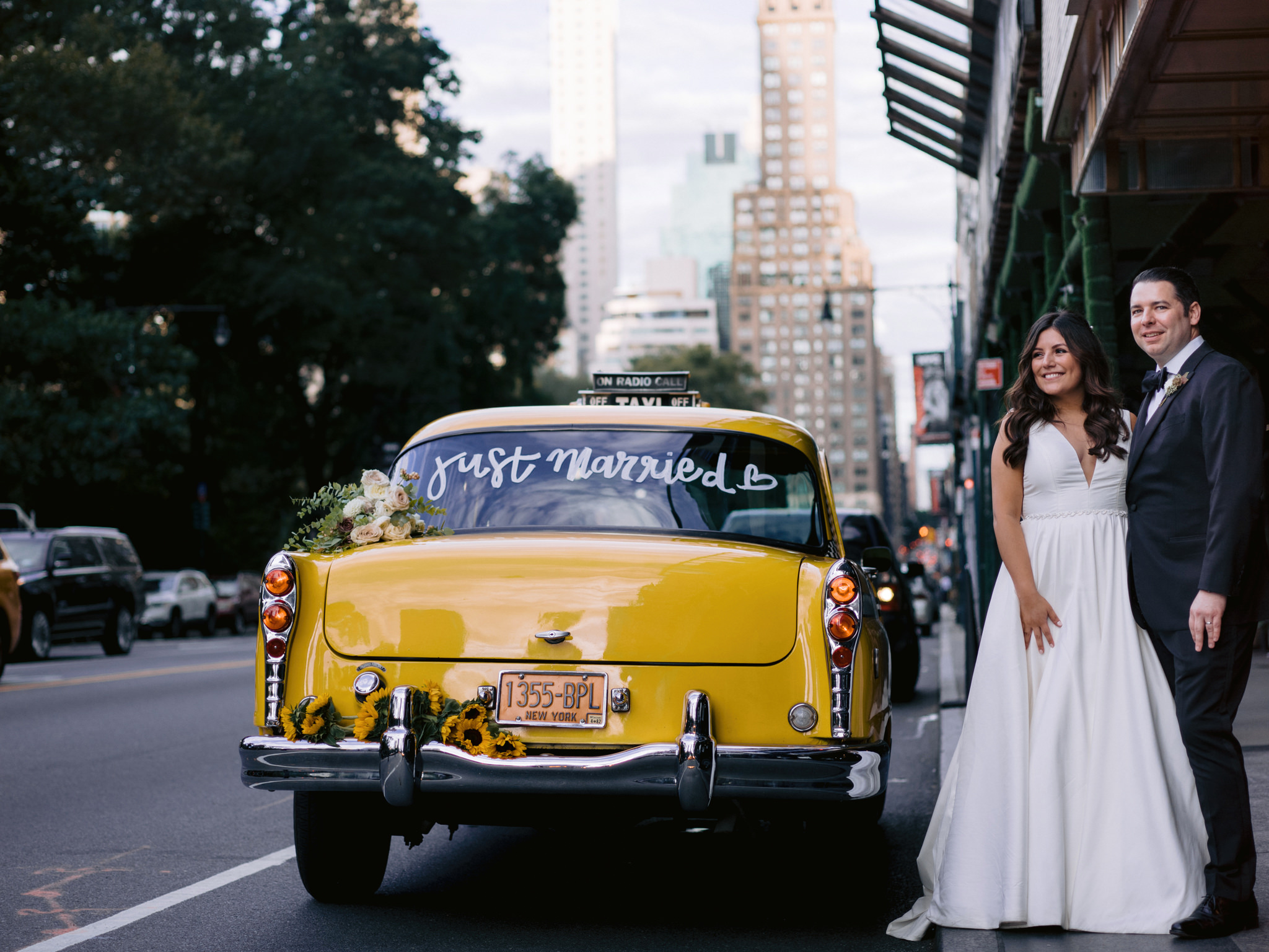 Bride and groom smiling in the street beside a vintage NYC taxi