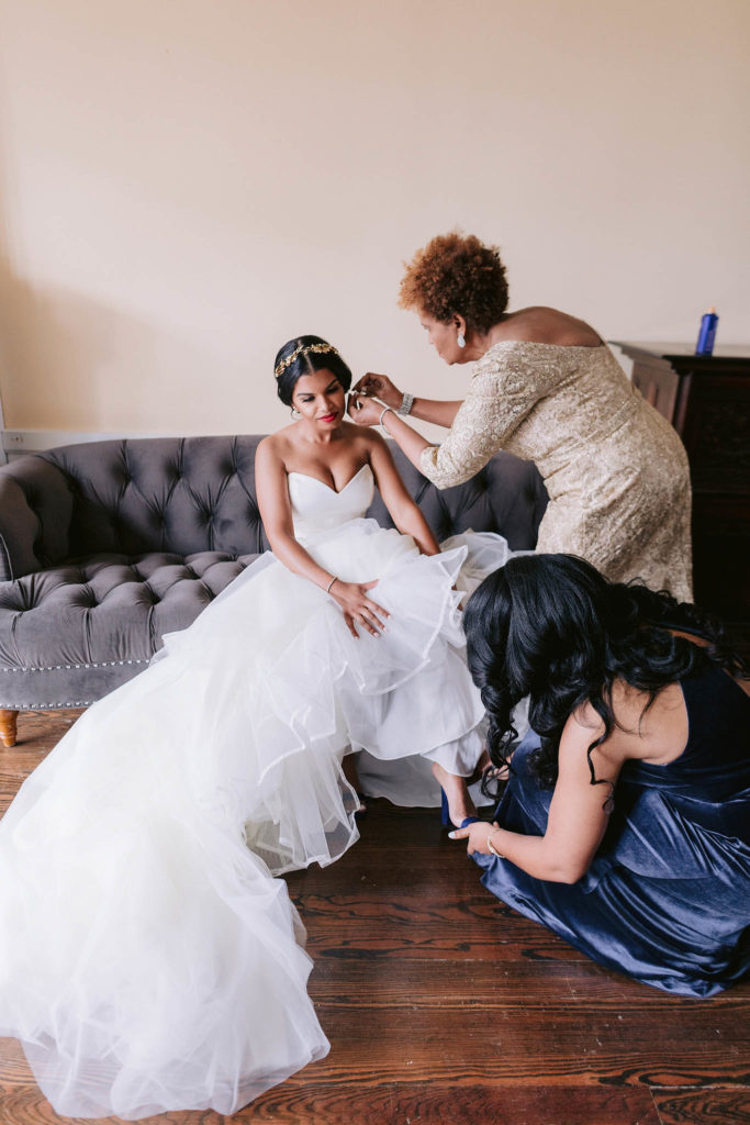 Bride is helped into her dress by her mom and her bridesmaids in a huge room flanked by windows in Castle Gould at the Sands Point Preserve in New York