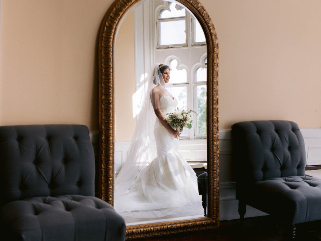Reflection of a bride in a mirror as she stands inside a room at Castle Gould in New York
