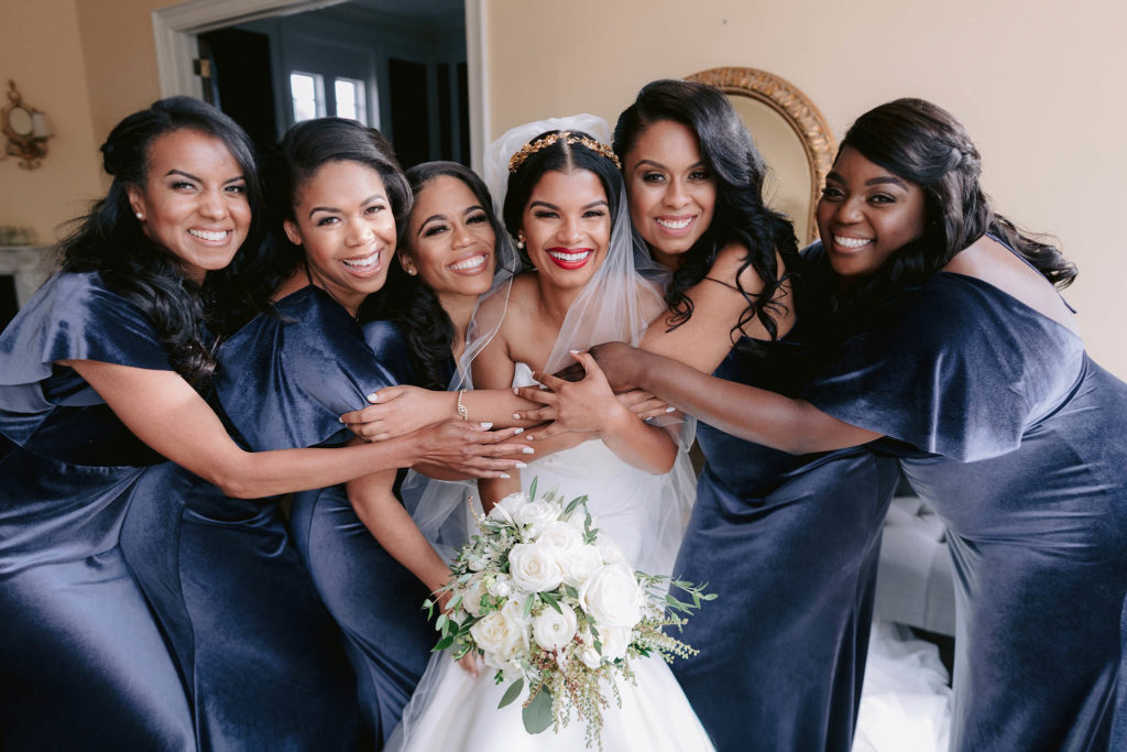 Bride is hugged by all her smiling bridesmaids in Castle Gould at the Sands point Preserve in New York