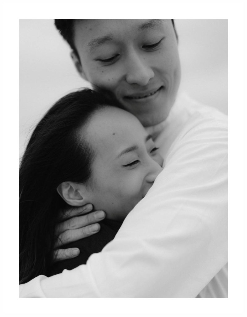 Happy Asian couple who is newly engaged hold each other close with their eyes closed and smiles on their faces. Photo by Jenny Fu Photographer