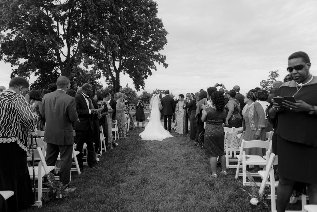 Happy bride walks down the aisle with her father in this outdoor ceremony at Castle Gould in NY