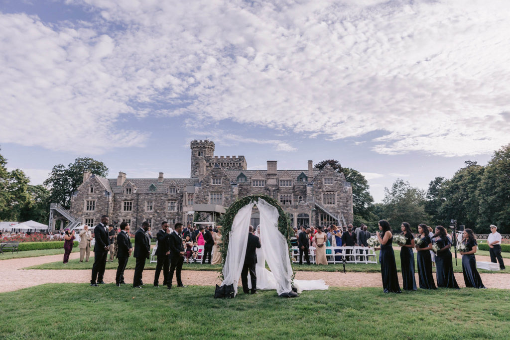 Wide angle shot of a wedding party and all guests with Castle Gould taking up most of the background of the photo in this outdoor new York wedding