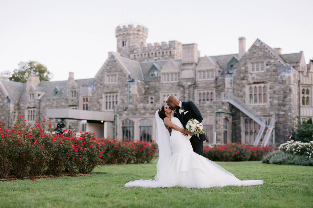 Groom dips his bride for a kiss in front of the enormous limestone Castle Gould located at the sands point preserve in New York