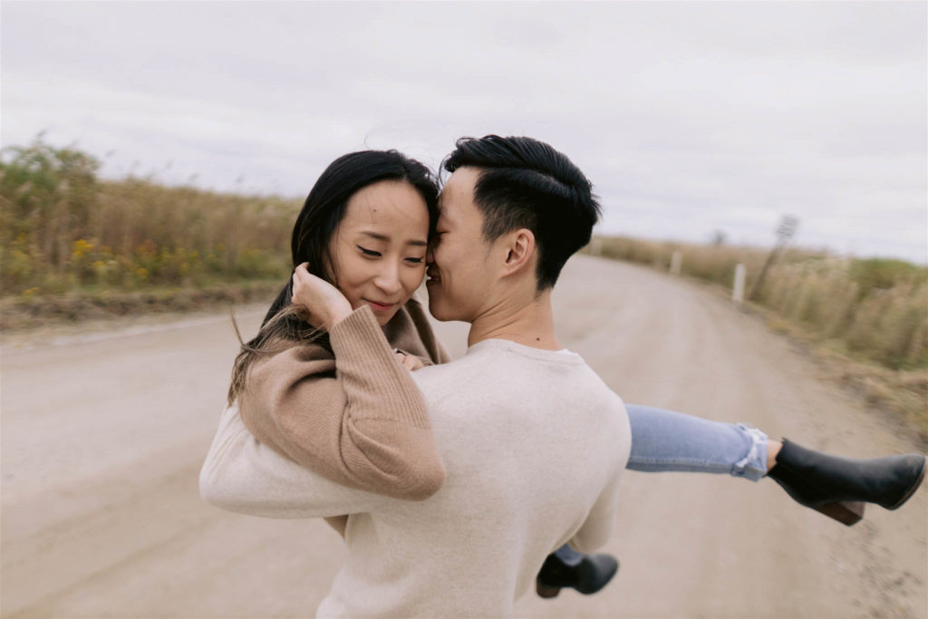 Asian man carries his Asian fiancee along the road and nestles his nose into her cheek in New York's fire Island