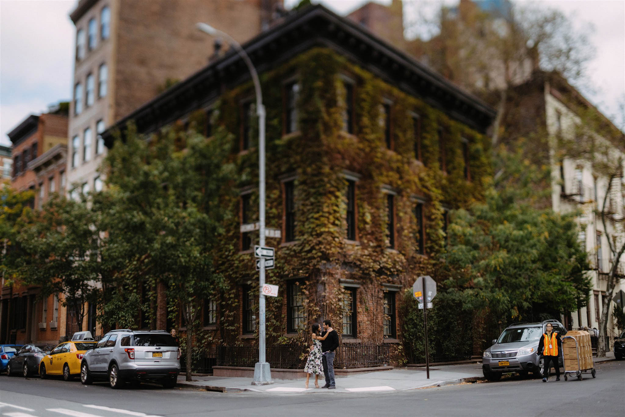 Engaged New York City couple stands before a famous NYC brownstone staring at each other and smiling