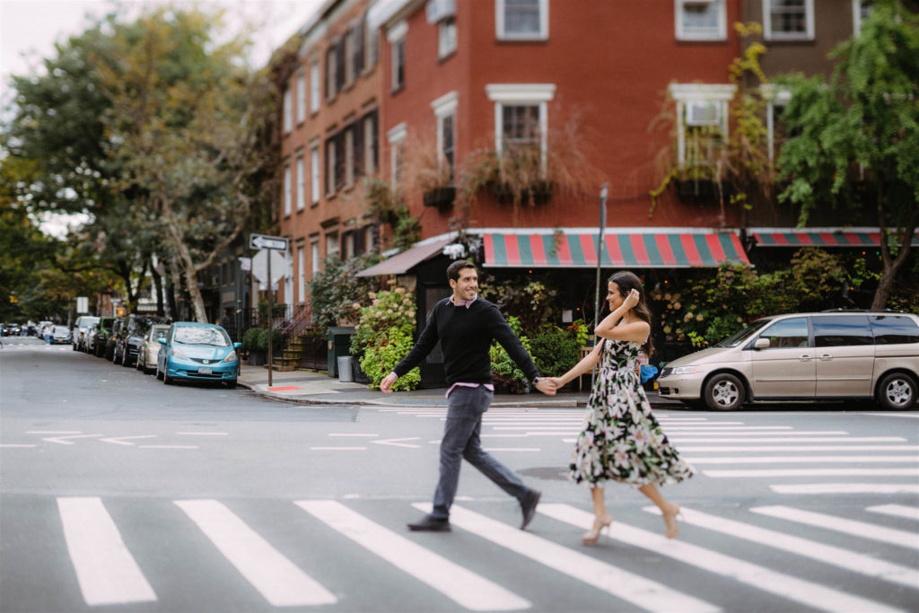 Young and attractive couple cross a street in the West Village of new York City, hand-in-hand, smiling at each other.