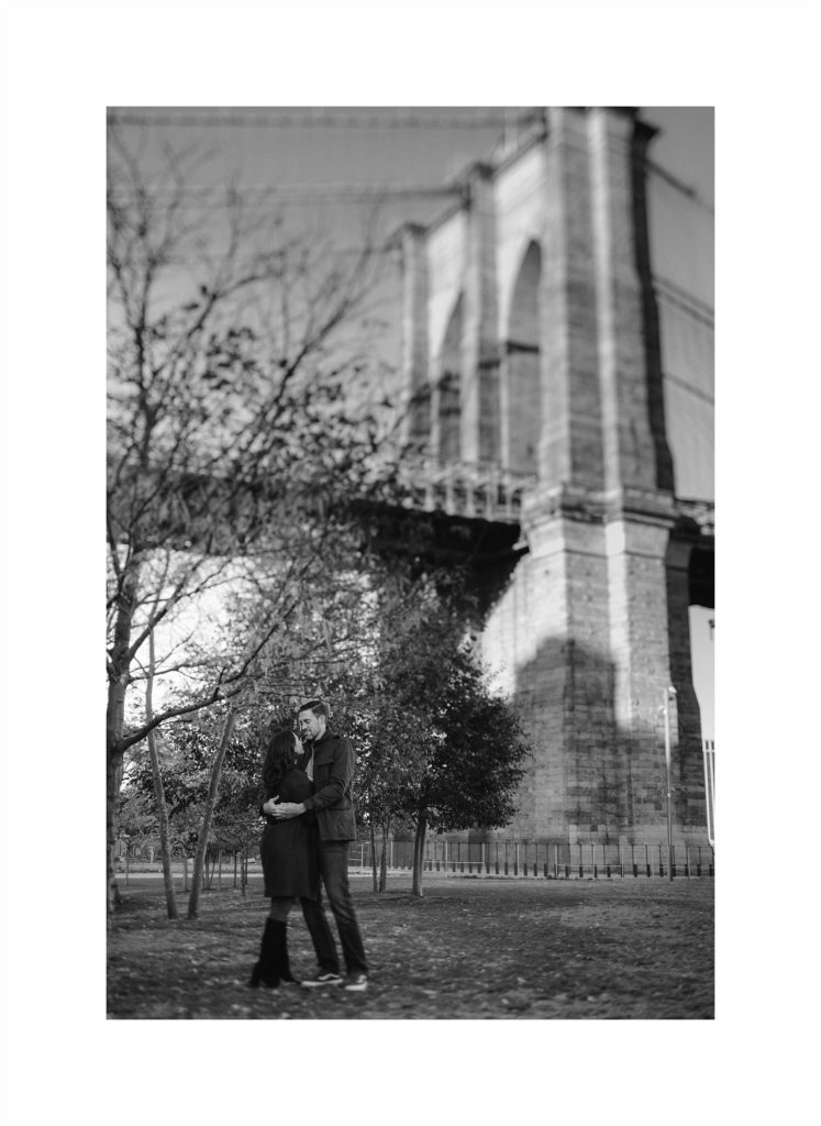 Couple snuggles up together under the Brooklyn Bridge, with an engagement session by Jenny Fu
