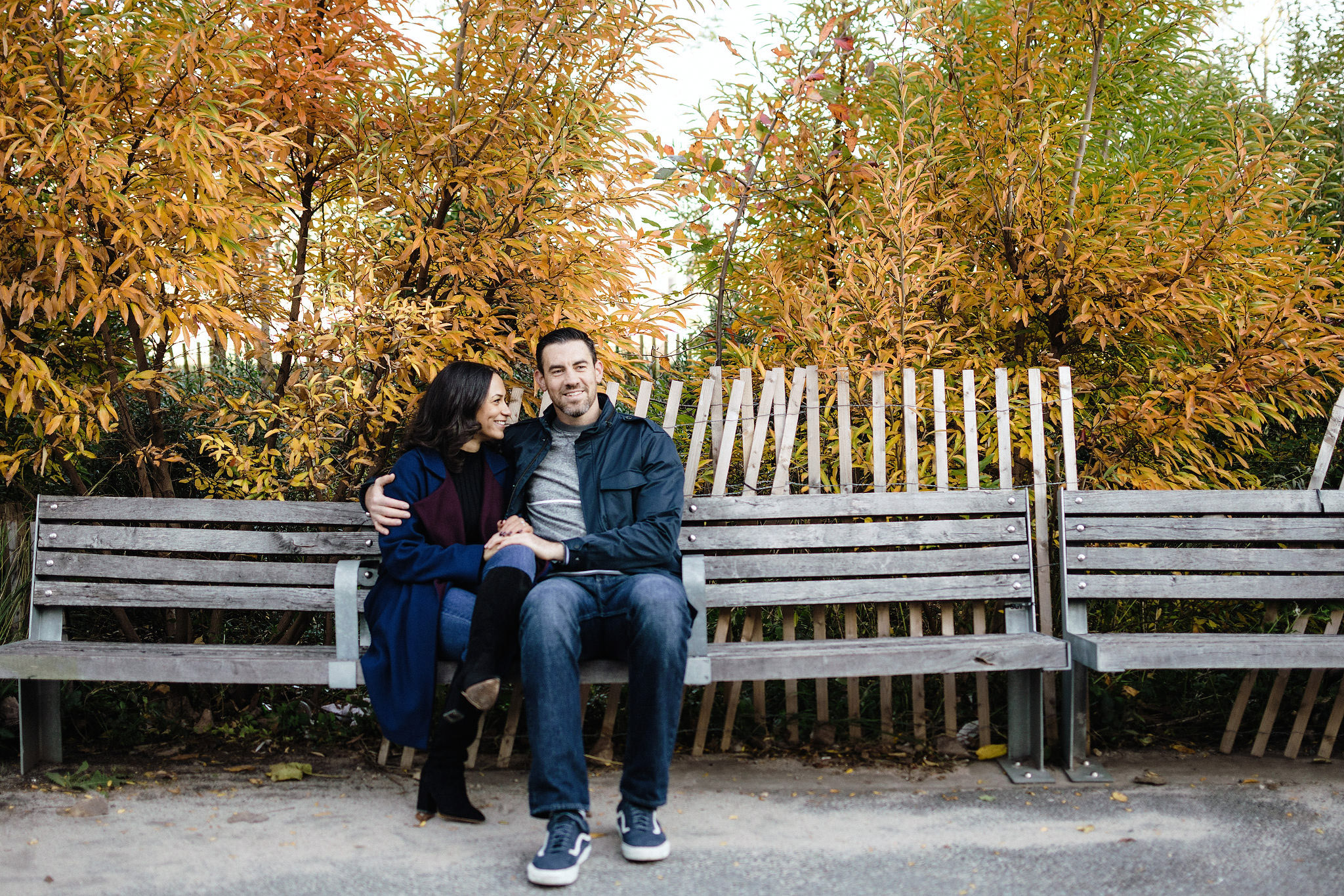 Engaged couple hang out on a park bench in Brooklyn Heights and giggle together