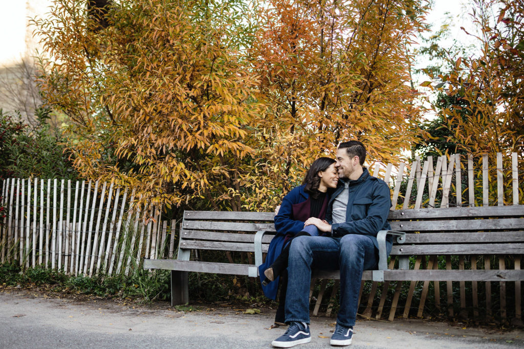 Cute engaged couple sitting on a park bench in the fall while the man kisses his lady's forehead