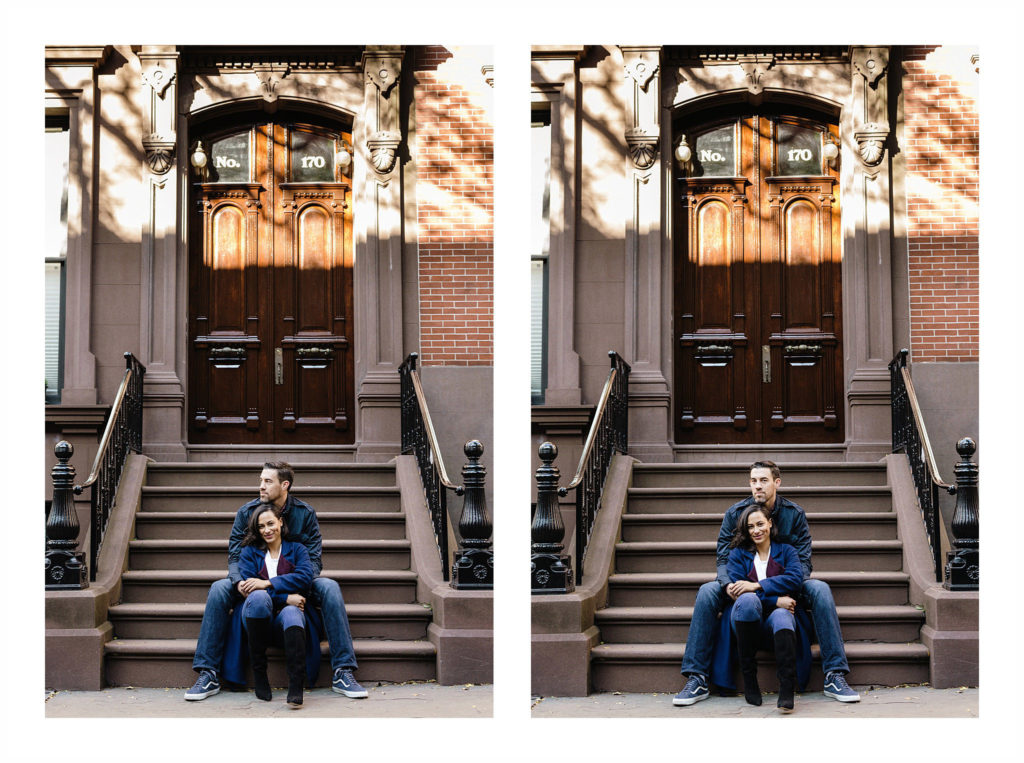 Engaged couple sits on the stairs of a brownstone, with her sitting between his knees while he wraps his arms around her and the sun spackles the brownstone behind them in Brooklyn Heights