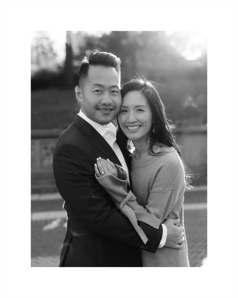 happy, attractive asian couple hugs with their faces together and her ring hand on his shoulder.