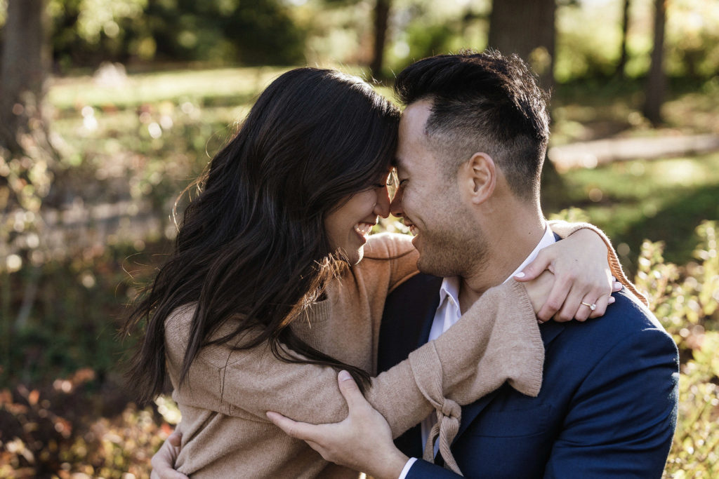 smiling, laughing asian couple who are newly engaged, hug each other in central park with their noses pressed together. beautiful enagagement imagery by Jenny Fu Studio