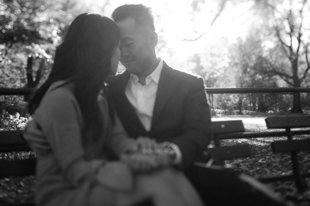 beautiful sunset shot of a newly engaged couple sitting on a park bench in central park with their foreheads pressed together and their eyes closed