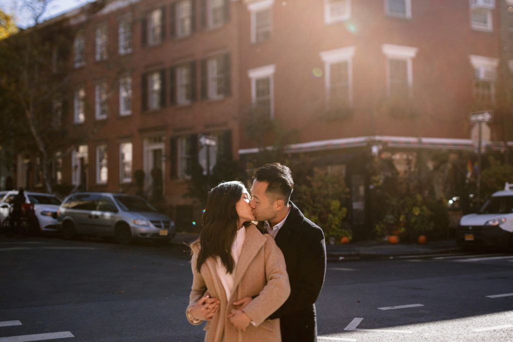 a happily engaged couple kisses on a corner in the west village in front of brownstones. image by jenny fu