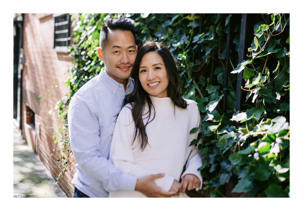 an attractive asian couple wearing chic casual, lean against a creeping vine in the west village, smiling for the camera