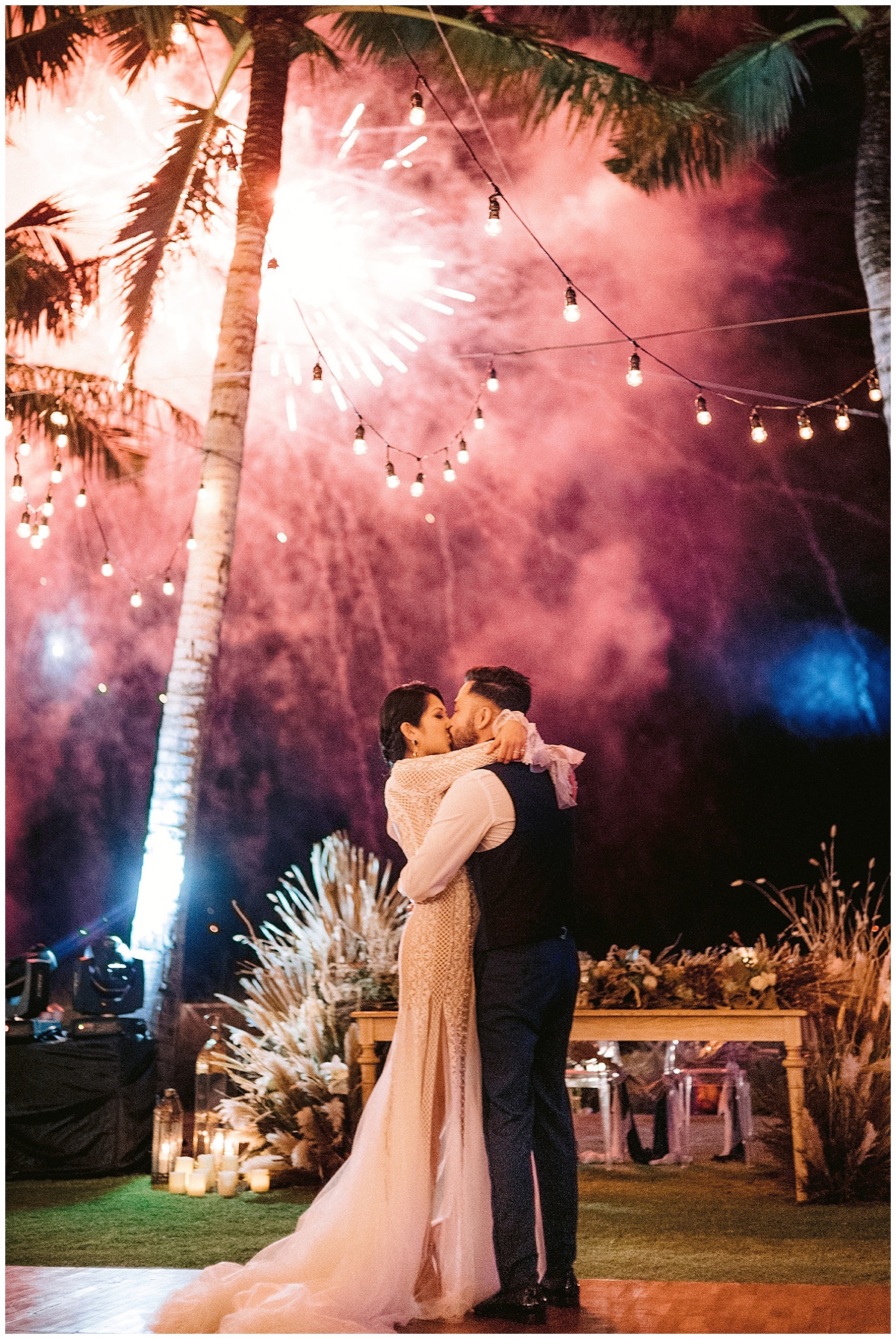 Bride and groom wrap their arms around each other and kiss underneath fireworks at their wedding in Bali. Editorial wedding image by Jenny Fu Studio