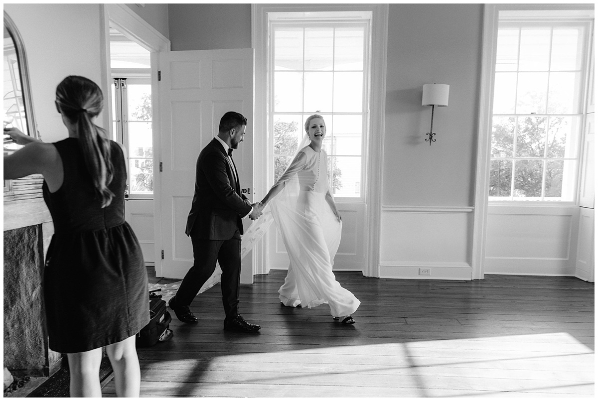 bride and groom enter a sunny room, hand in hand, smiling and celebrating their first moments as husband and wife. Photojournalistic image by Jenny Fu Studio