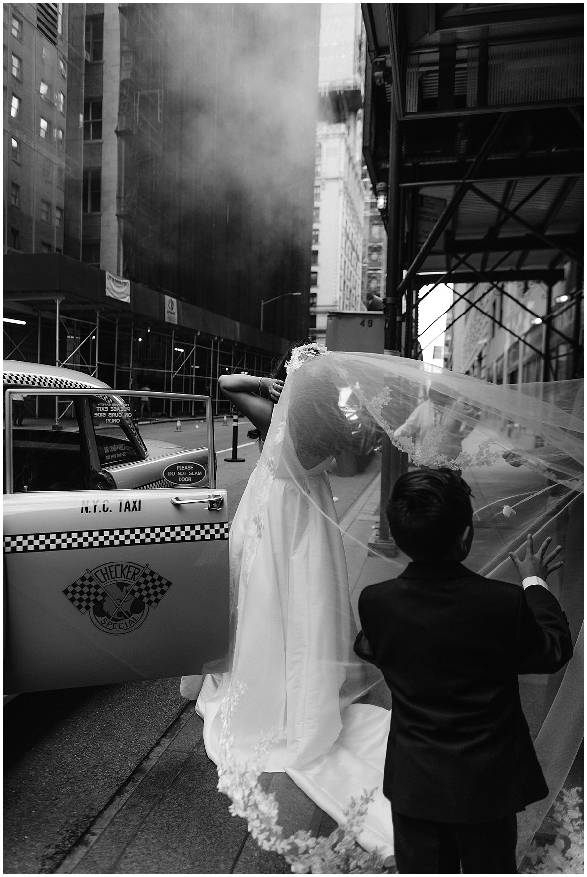 A bride gets into a yellow cab in New York as her veil blows in the wind and her ring bearer tries to catch it
