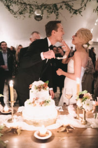 bride and groom feed each other cake and laugh together as the bride smears it on his chin. Image by Jenny Fu Studio. Editorial Wedding at Firefox Mountain House in Upstate New York.