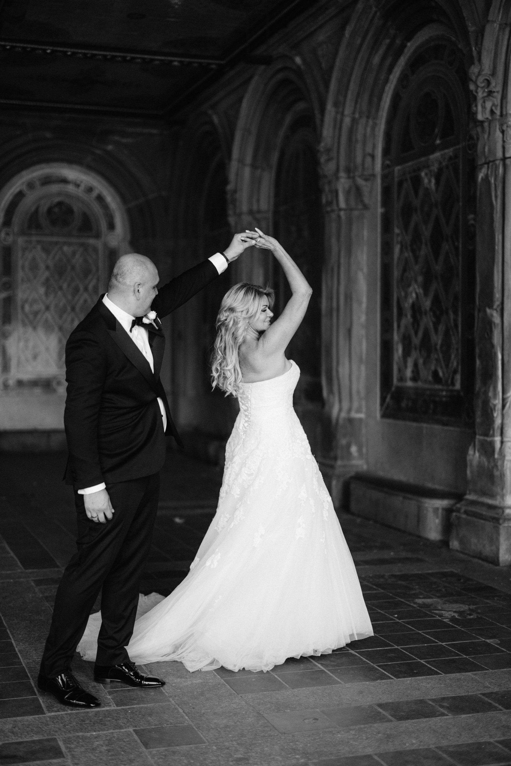 Man twirls his wife in her wedding dress, in a New York City cathedral on their wedding day
