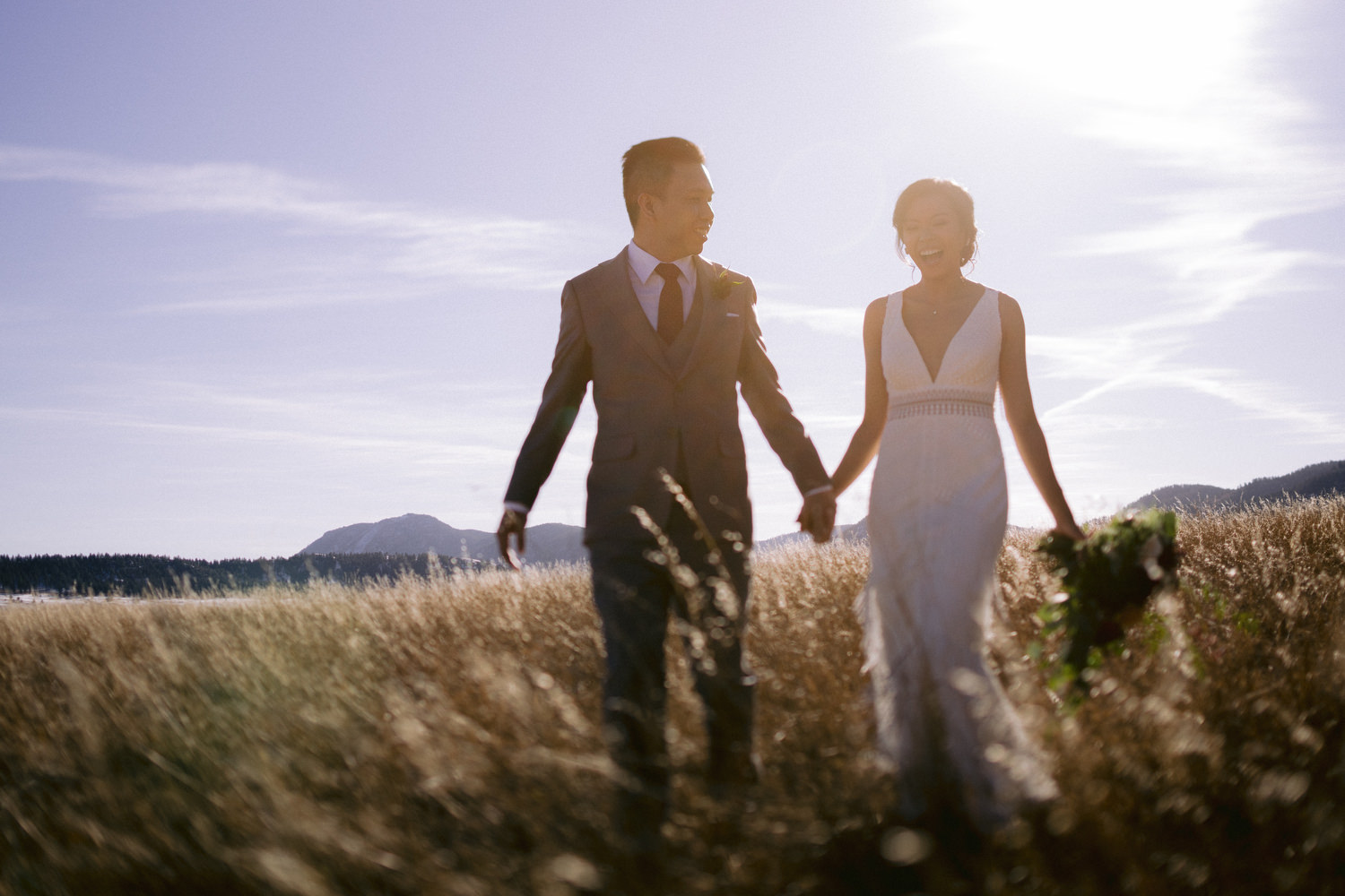 Couple holding hands walking through tall grass on their wedding day at Spruce Mountain Ranch