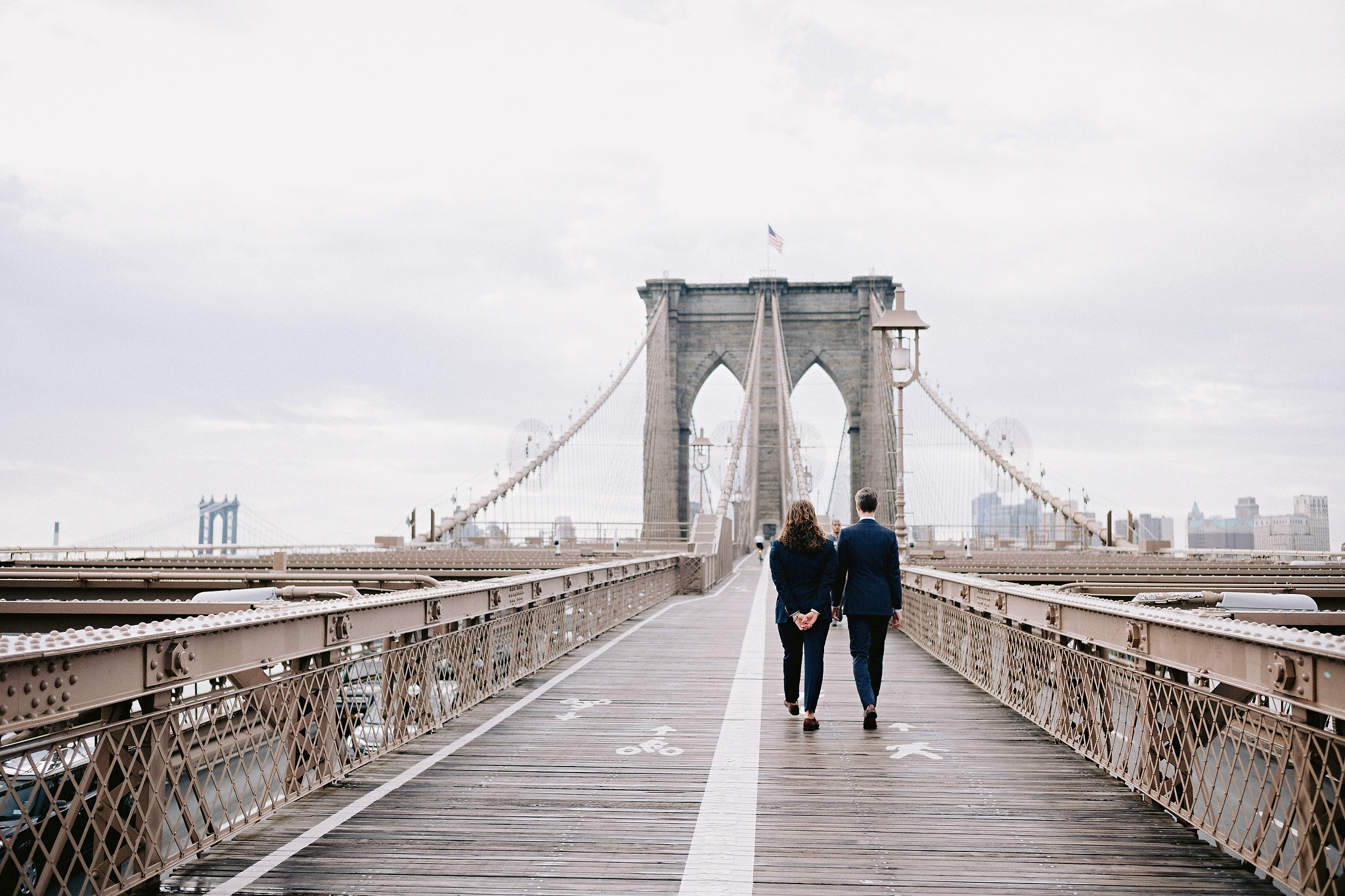 Husband and husband walking across the Brooklyn Bridge after their city hall wedding