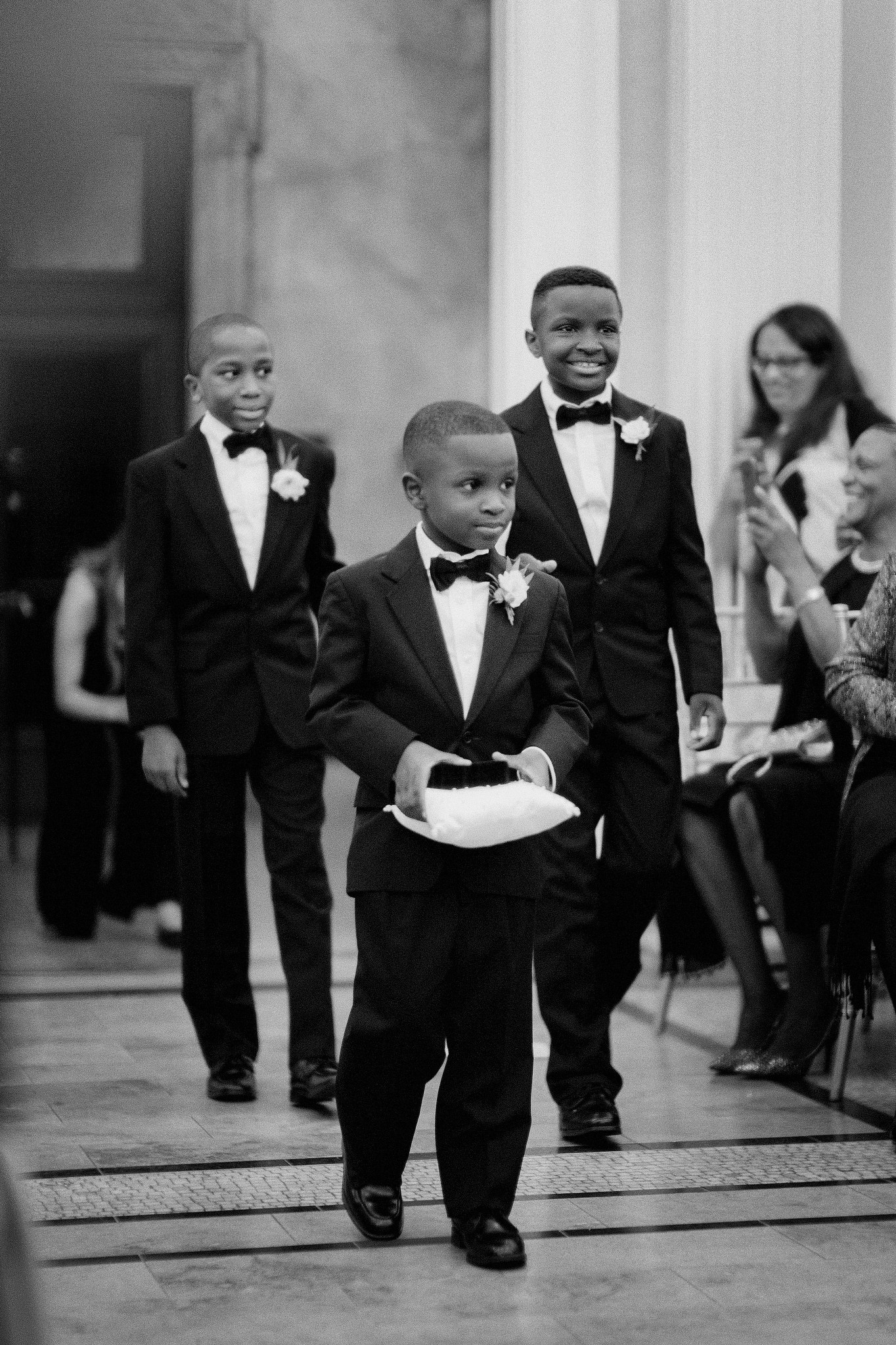 Three young boys in suits walking down the aisle, ring bearer in front at wedding