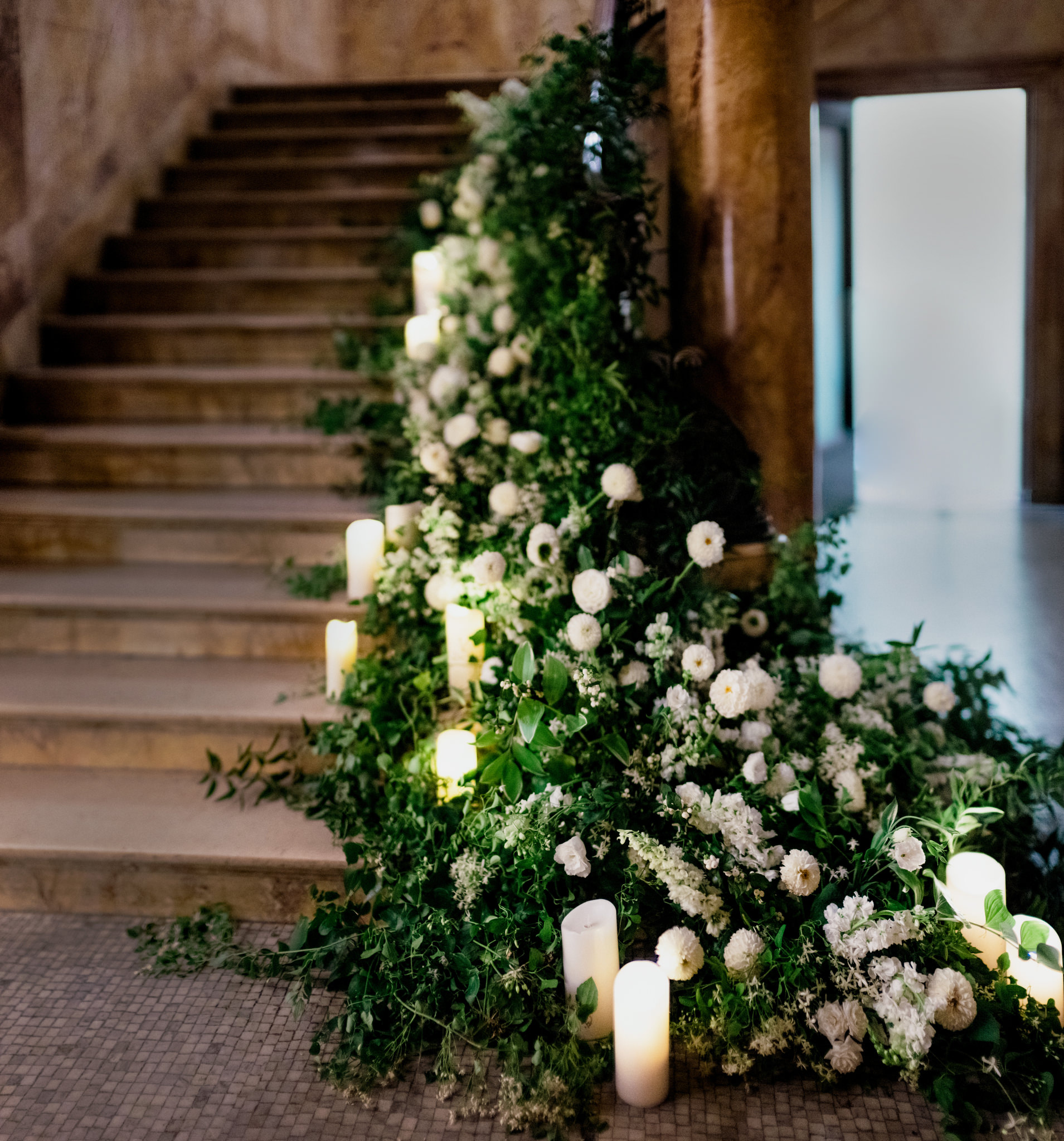 Beautiful staircase at Providence Public Library lined with white flowers, candles, and green foliage for wedding photographed by Jenny Fu
