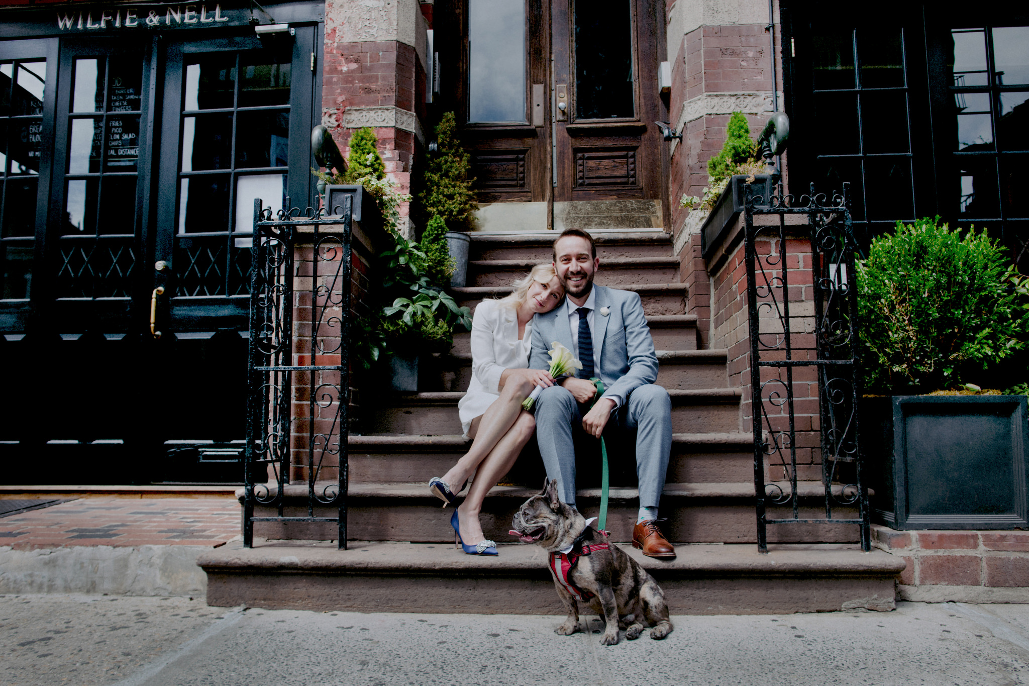 Bride and groom sitting on steps of old building with their dog on wedding day in New York