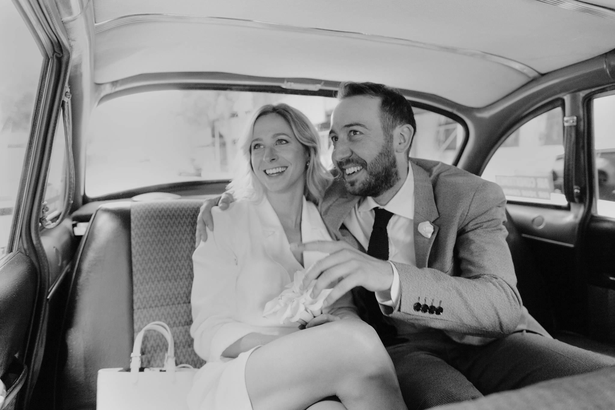 Couple smiling sitting in back seat of yellow taxi on wedding day