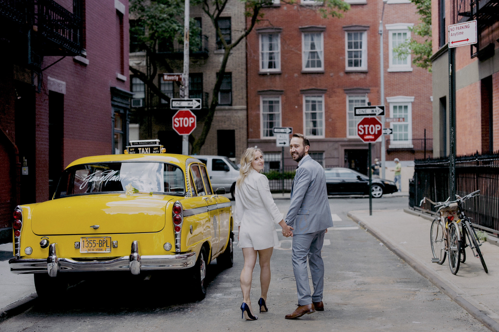 Married couple on their wedding day looking back with vintage taxi with Just Married written on the back window.