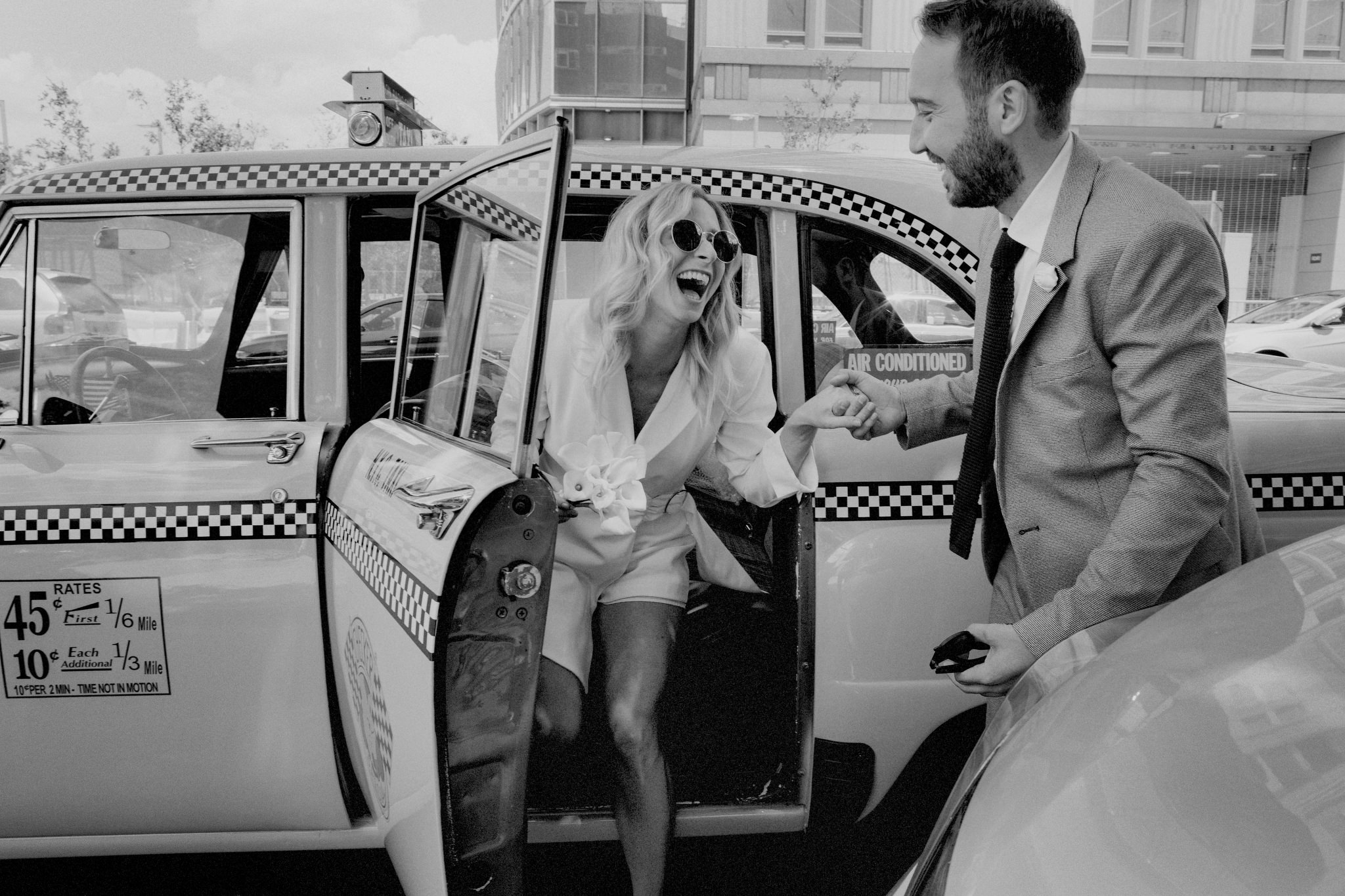 Newly married couple exiting a vintage taxi. Groom helping the bride out of the car with big smiles.