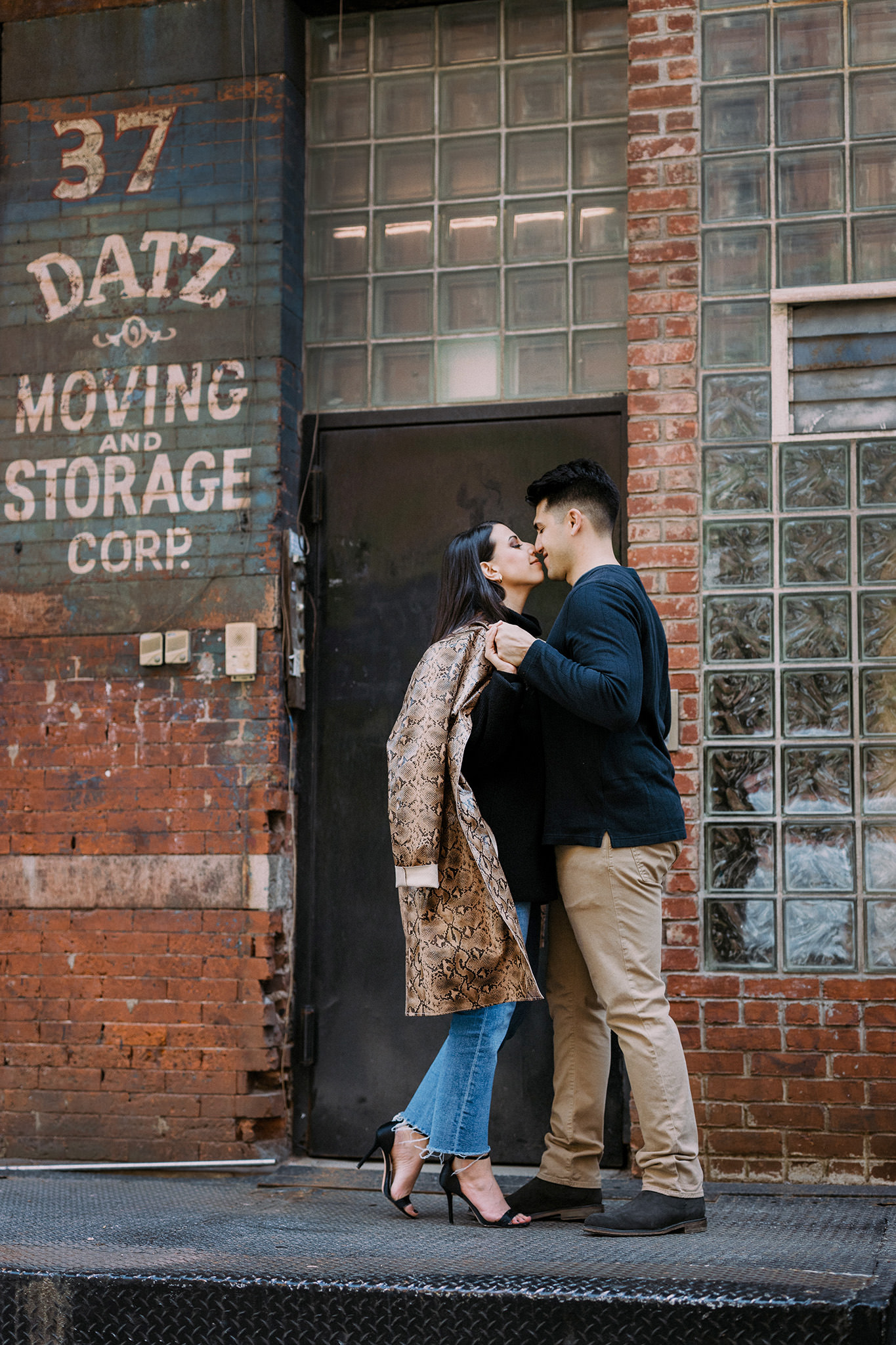 Couple about to kiss in front of old brick building with Datz Moving and Storage Corp sign