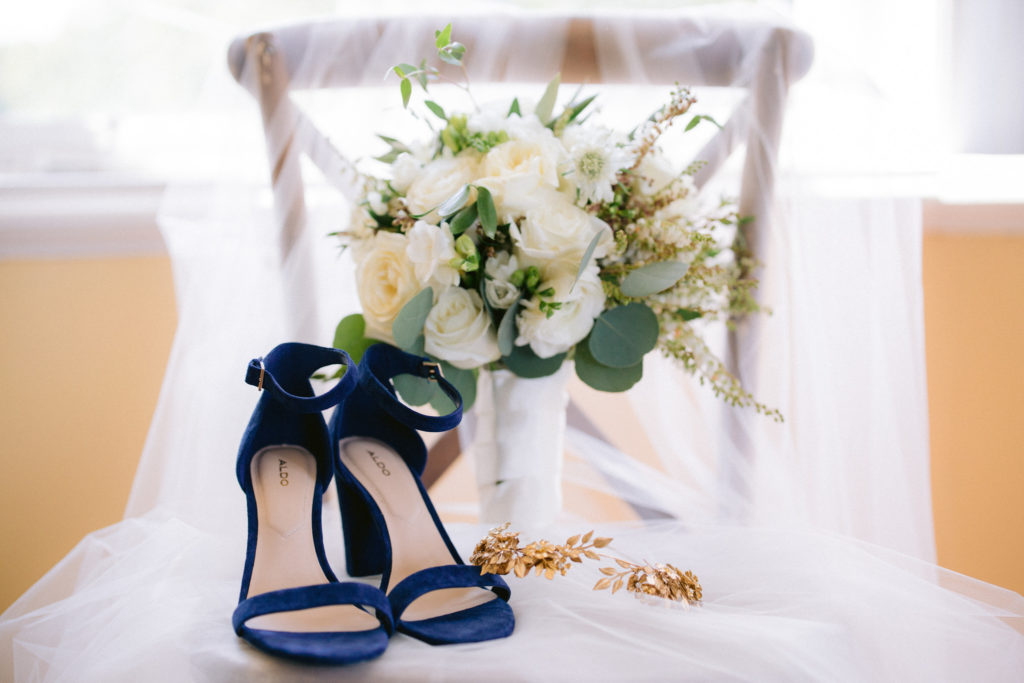 Bridal veil draped on chair with blue heels, green and white bouquet, and gold etsy crown