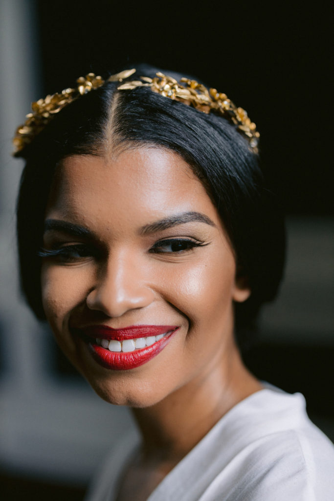 Bride smiling wearing red lipstick and gold crown on wedding day